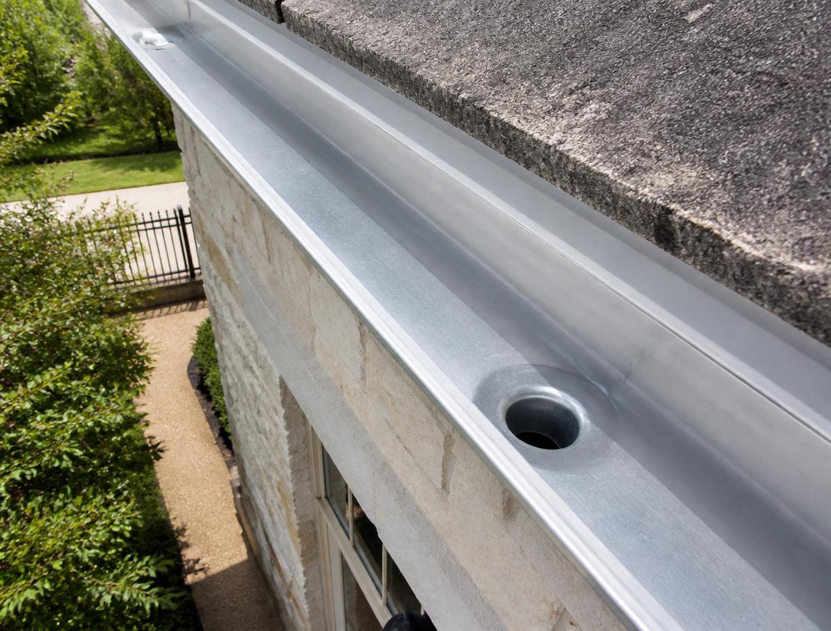 Same gutter cleared to bare metal with clean downspout opening after cleaning